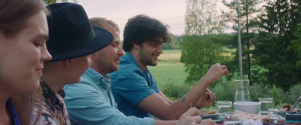 Group of friends eating and talking sitting at a table near a grass field at sunset