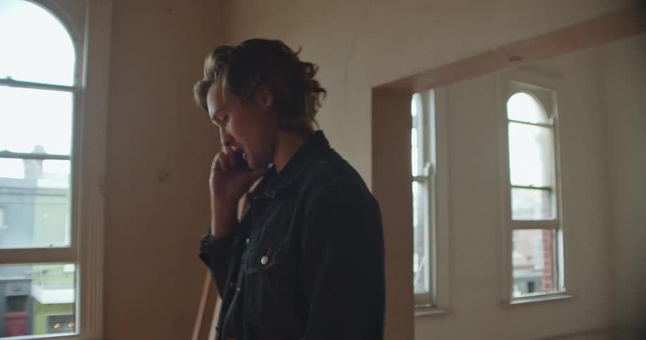 Man with denim jacket talks on smartphone in empty room