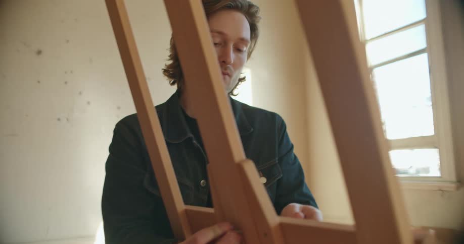 Man puts in screw in wooden easel standing in near empty room