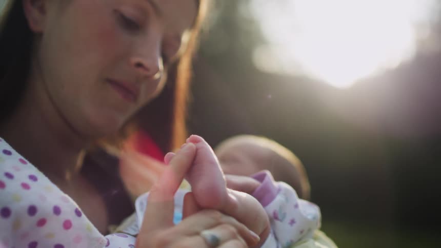 Mother caressing the foot of a newborn baby under the morning sunlight
