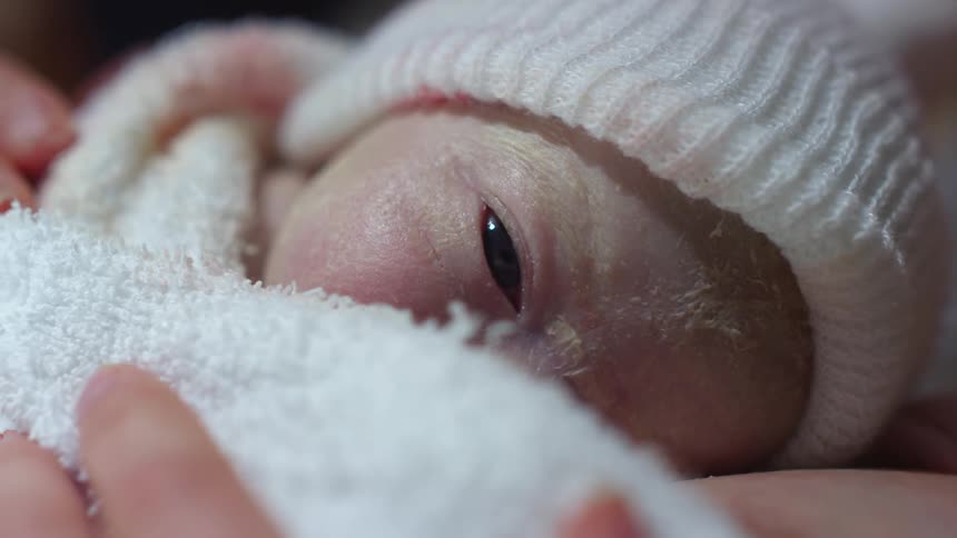 A newborn baby wrapped in a blanket sleepily blinks their eyes