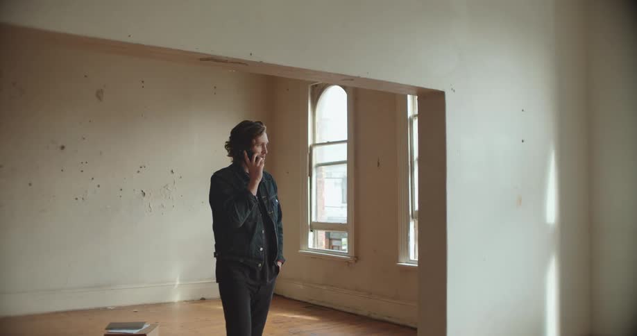 Man talking on the phone standing over the hardwood floor of an empty apartment