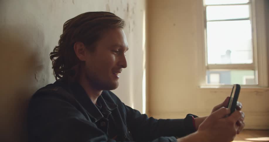 Man sits on the floor and does a video chat and holds up the phone to show the room to the person hes chatting with