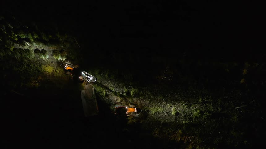 Tractor with headlights on pulling a cart between the crops on a farm at night