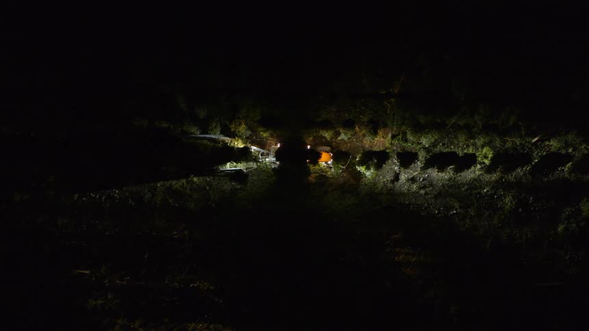 A tractor drives through a field of crops at night