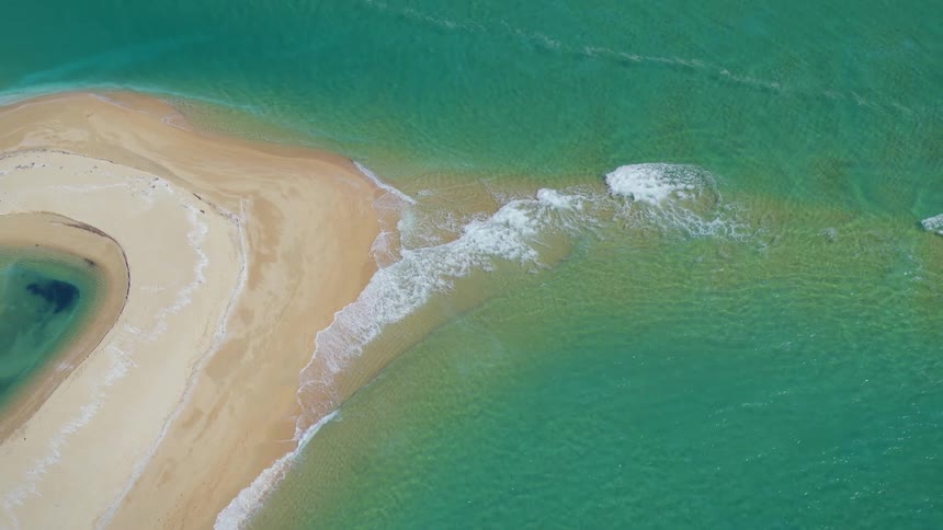 Aerial view of a sand atoll on the green ocean waters