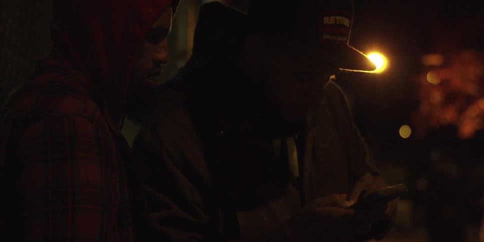 Two men are talking and checking a phone at night