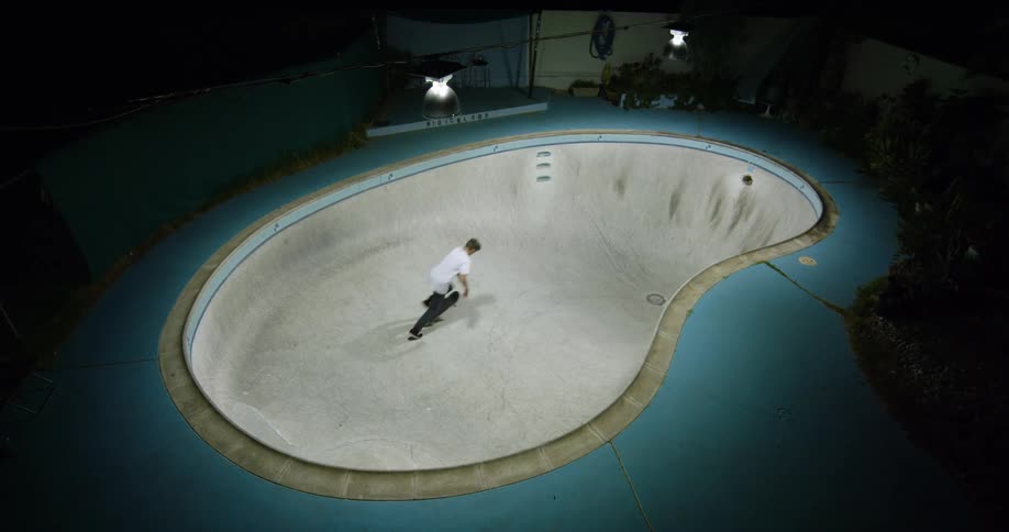 A man with a skateboard skating in an empty swimming pool