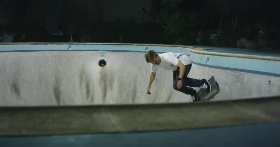 Young man riding a skateboard inside a pool at night