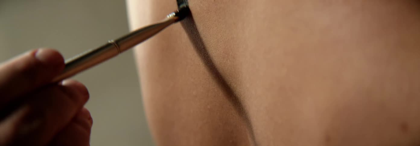 A view of someone painting a line on someones skin