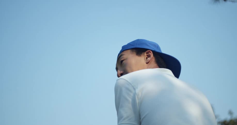 An asian man that appears to be getting ready to swing a golf club turns his head and talks