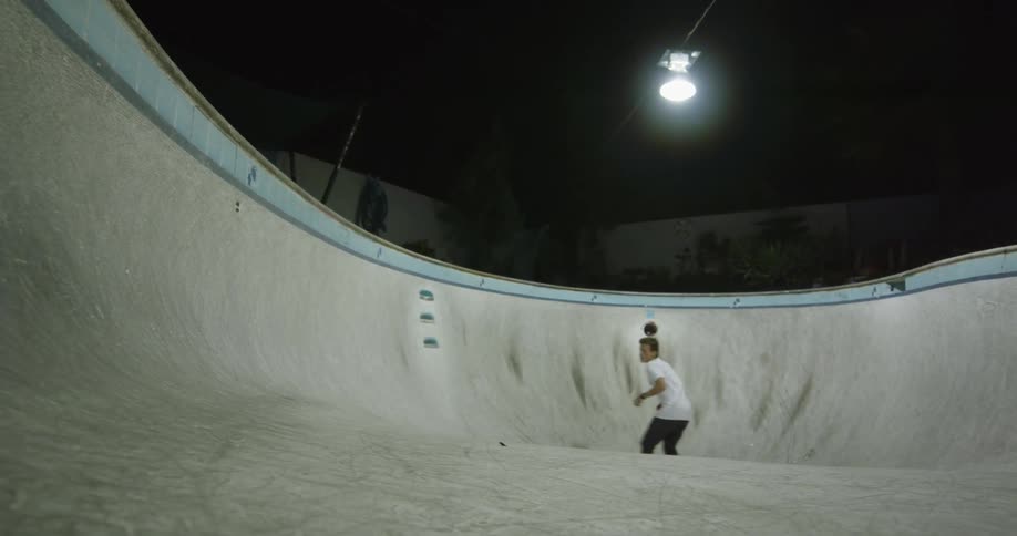 A man is riding his skateboard in the empty swimming pool