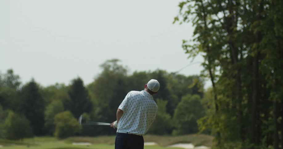 A man on a golf course swings his club and looks out into the distance