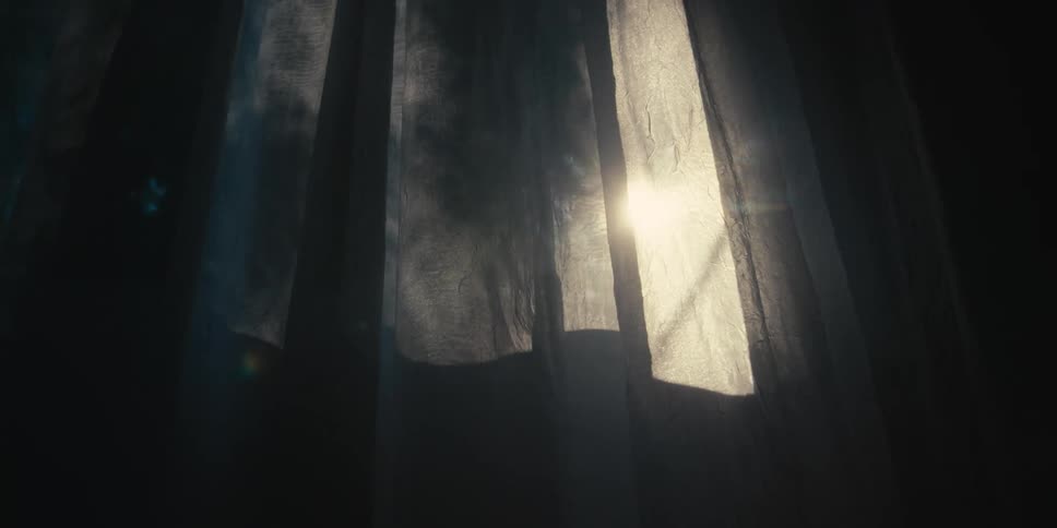 The sun shines through dark curtains