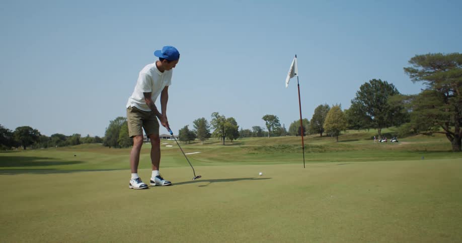 A man on a golf course putts a golf ball towards a nearby hole