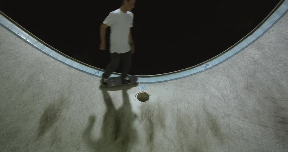 Young man skateboarding along the edge of an empty pool at night