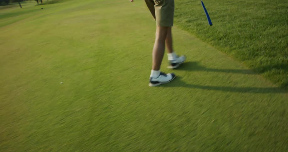 A man with a golf club walking on a golf course with trees the sky and clouds in the background