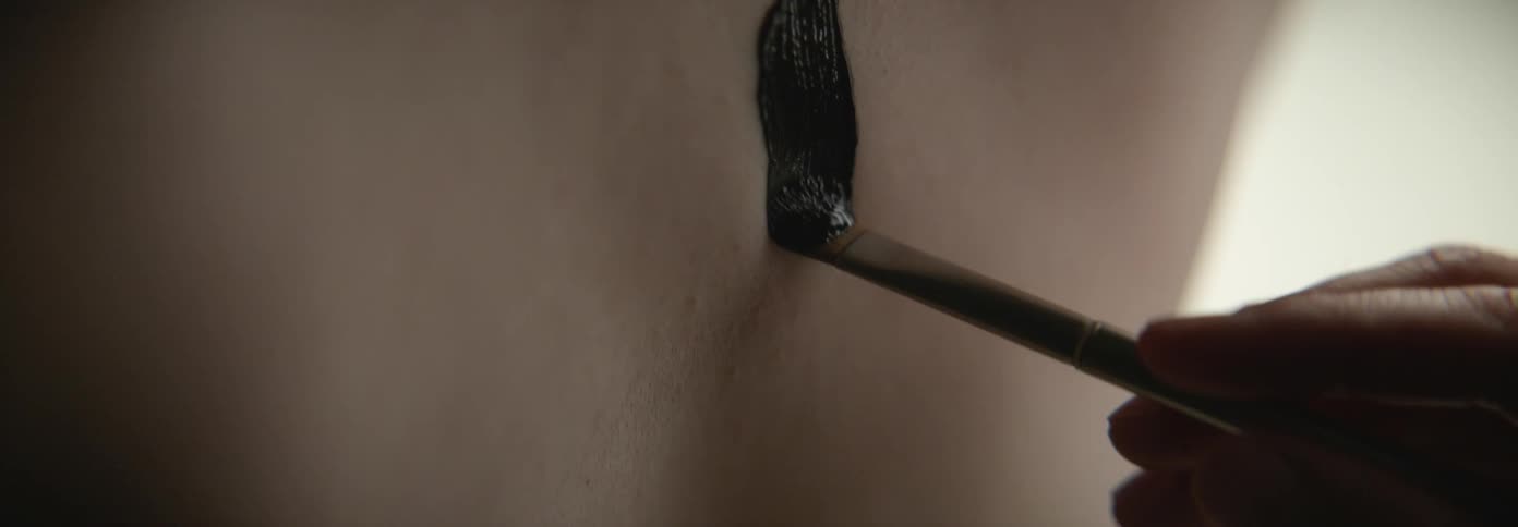 A hand holding a paint brush is painting someones back