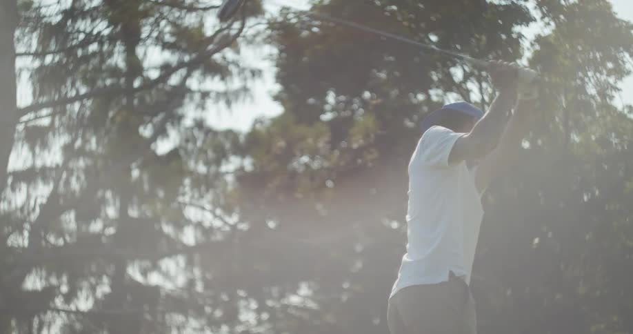 Young asian man swinging a golf club near the trees at morning