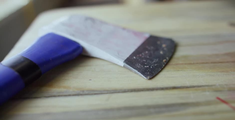 Axe with a blue handle and wood chips on the blade resting over a wooden table