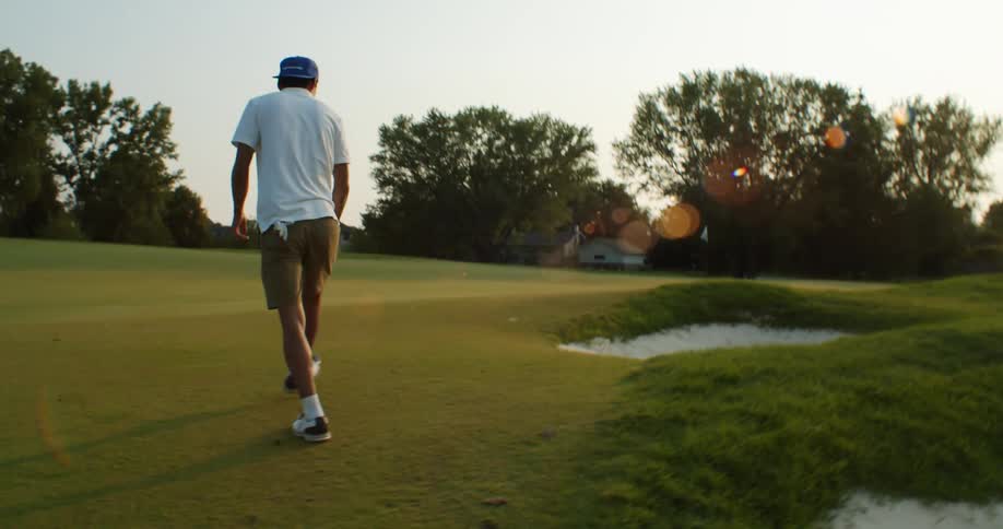Young golfer jumps out of a sand trap in a golf course at sunset