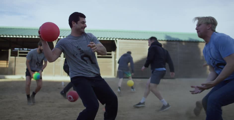 Group of men pick up colored balls and throw them at each other as they laugh and smile