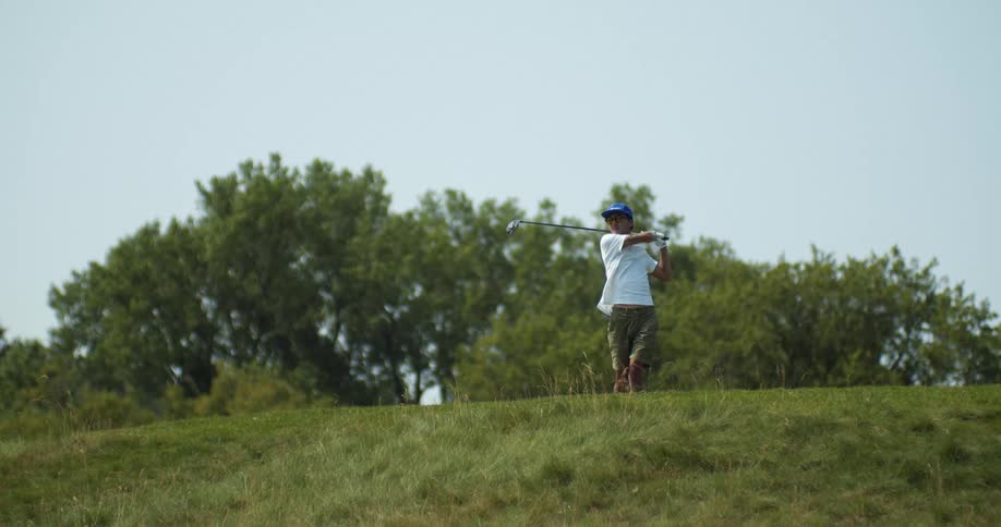 Man with cap white shirt green shorts hits golf ball with golf club