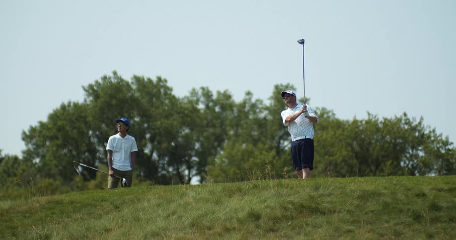 A golfer swings from the top of a small hill