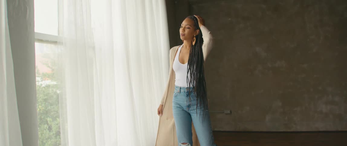 Woman stands in empty room near curtained window swaying and moving while smiling