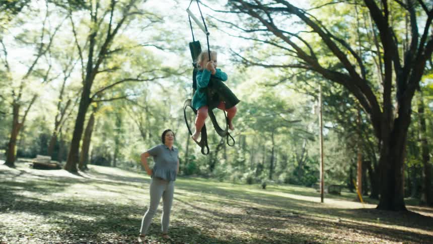 Toddler girl is smiling and swinging while woman happily watches