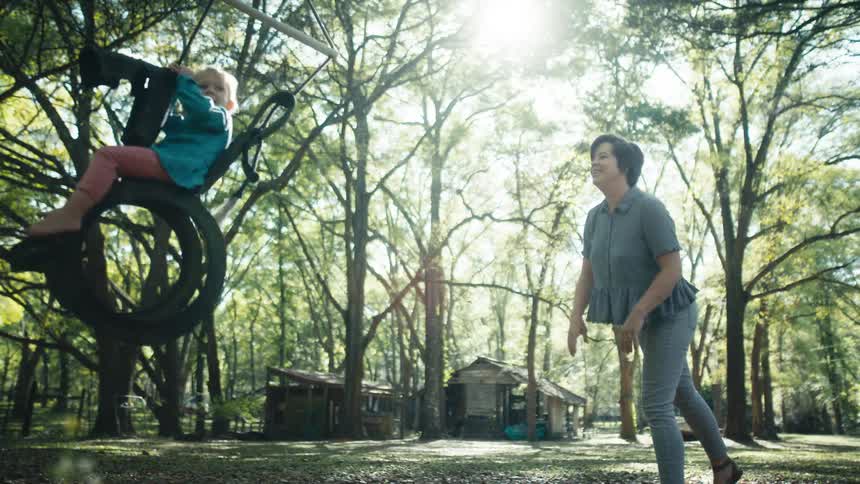 A woman is pushing a small child on a swing hanging from a tree