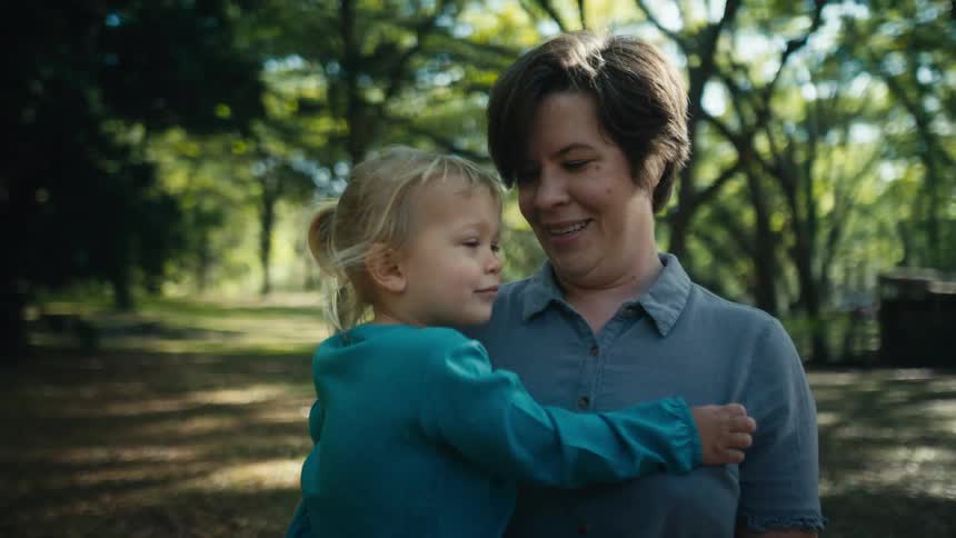 Woman holds girl in her arms swaying back in forth while standing in field surrounded by woods