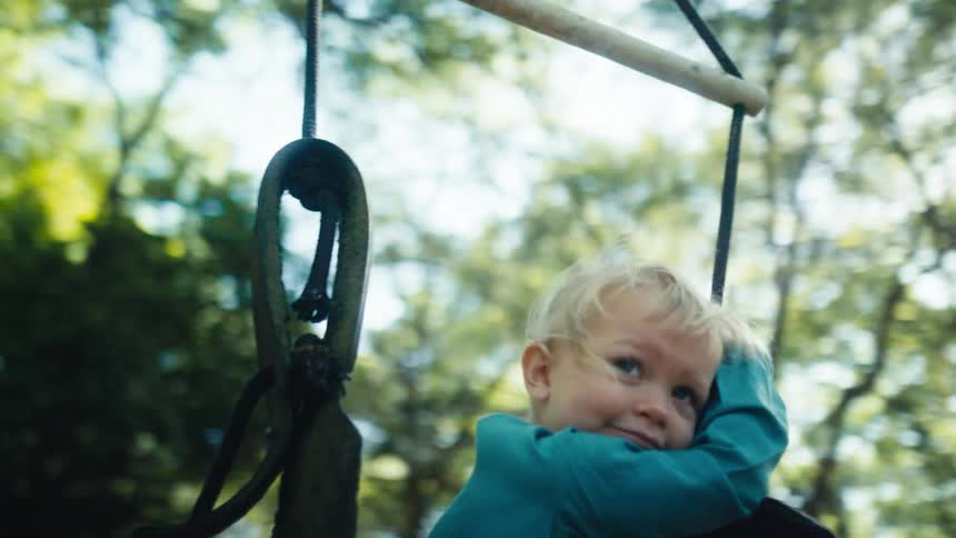 A girl swinging on a swing with trees the sky and clouds in the background
