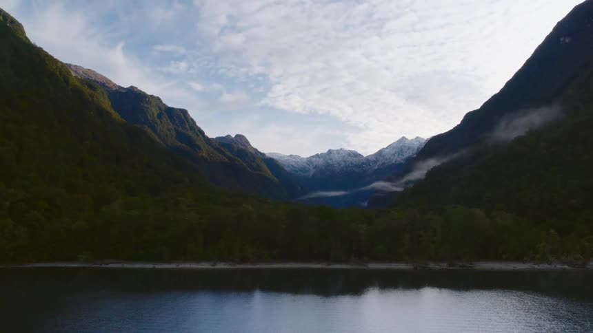 Lake surrounded by mountains under a hazy cloudy sky
