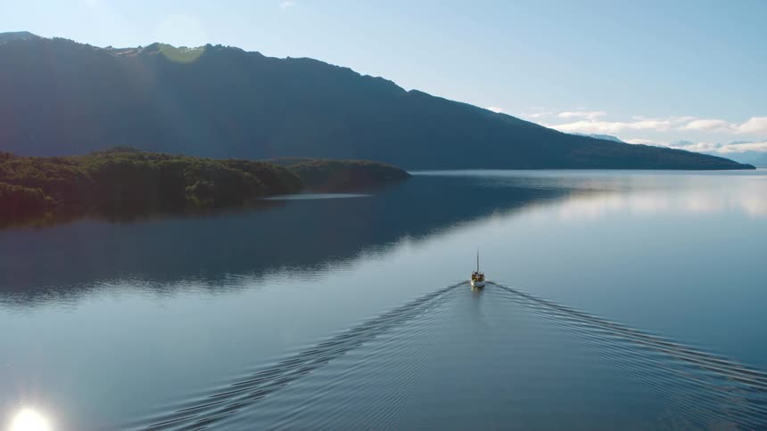 Boat driving over the calm surface of a lake near the mountains at morning