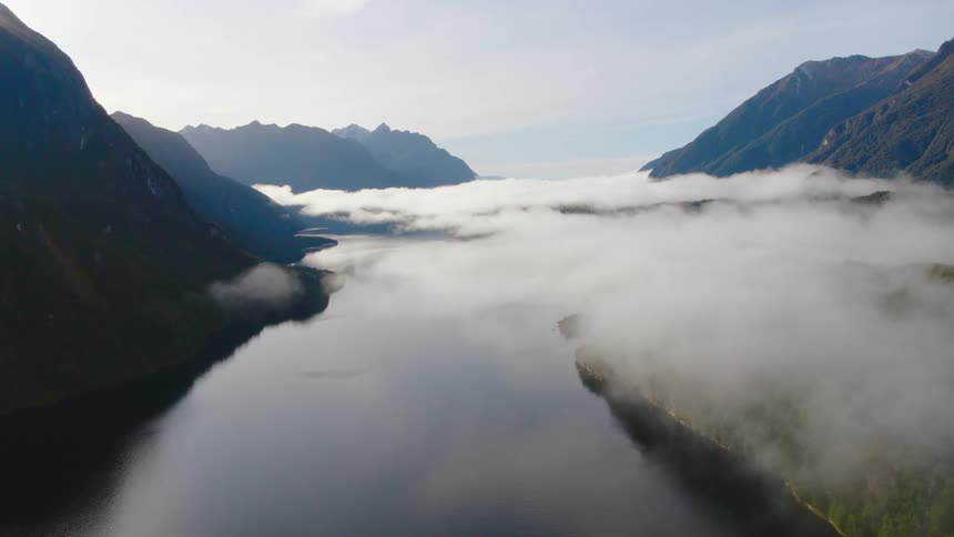 An aerial view of fog covering a river alongside a mountain range