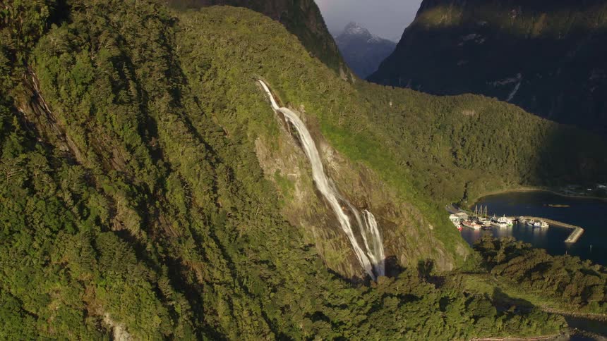 Water rushes and flows down a mountain slope into a lake where boats are docked