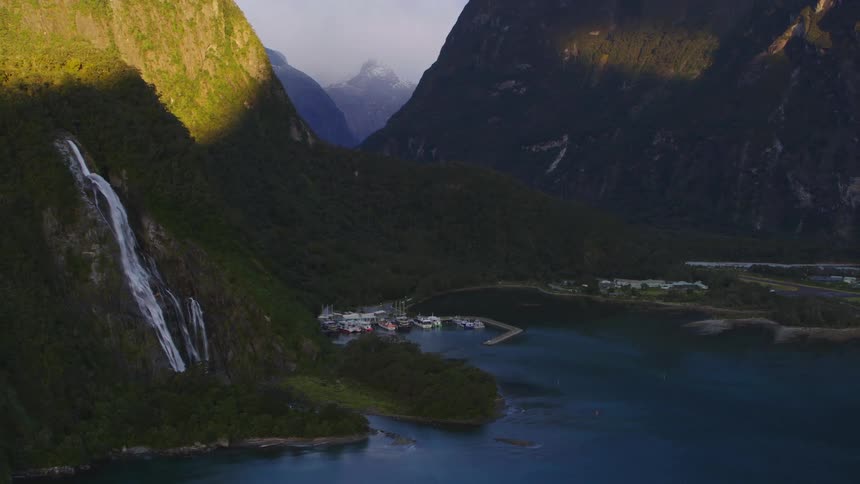 Water flows down a mountain slope into a lake where boats are docked at a pier