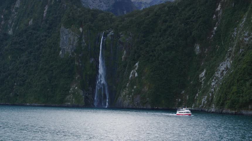A ship sails past a waterfall on a cliff
