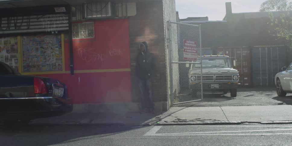 A man stands against a wall in a run down neighborhood