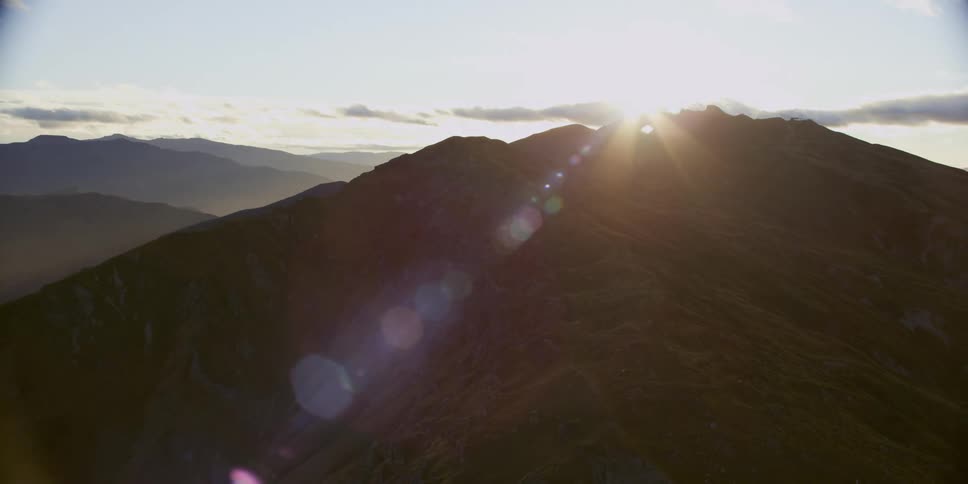 A mountain range with the sun and sky in the background