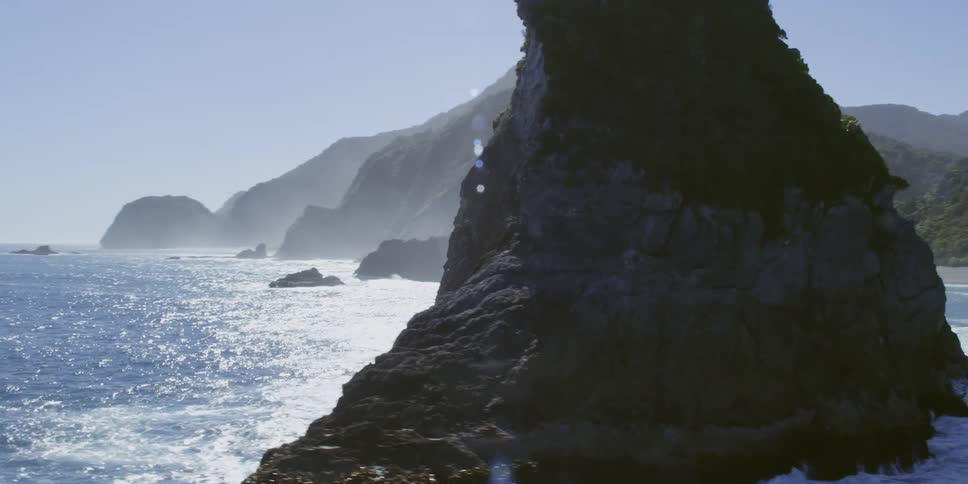 Aerial of small waves crashing onto large rock formation in the ocean