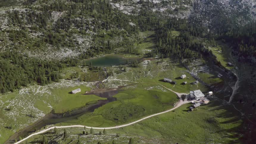 Road winds across valley containing river and lake toward large house near forested slope