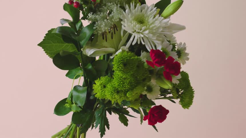 A bouquet of flowers with plants and leaves in a room with a wall in the background