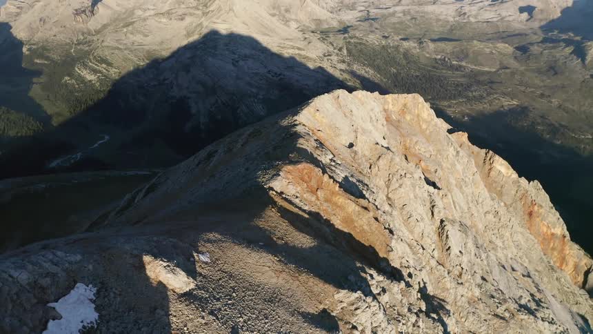 Sun shines onto face of craggy mountain casting shadow onto valley and nearby mountains