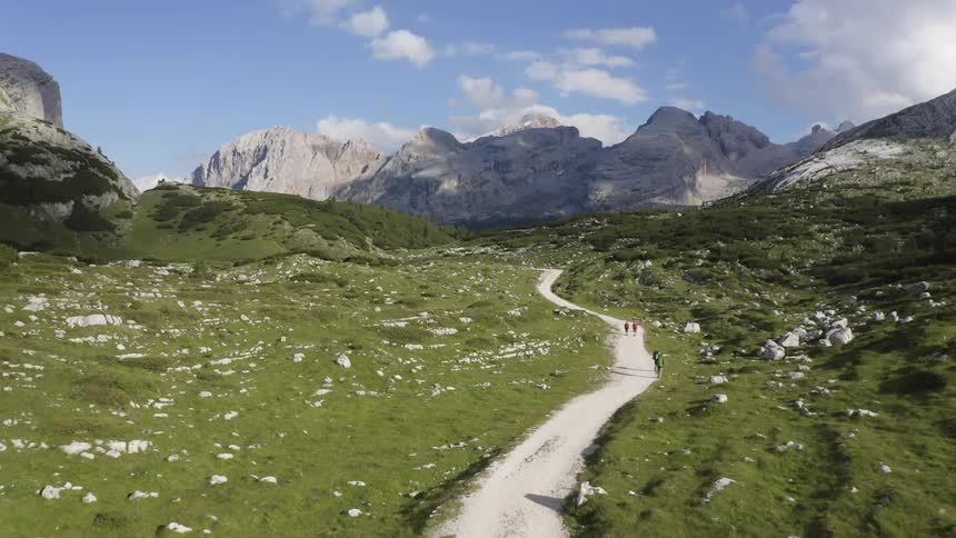 People hike on a trail running through a lush green field in a canyon