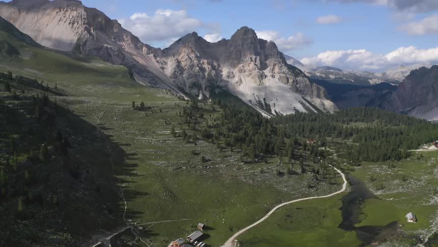 Aerial view of small village on mountain slope next to country road with high mountains in the background