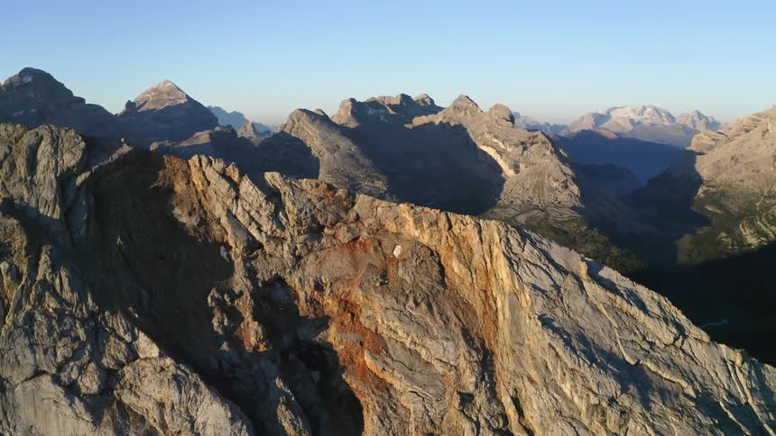 The camera flies away from a jagged range of rocky mountains on a sunny day