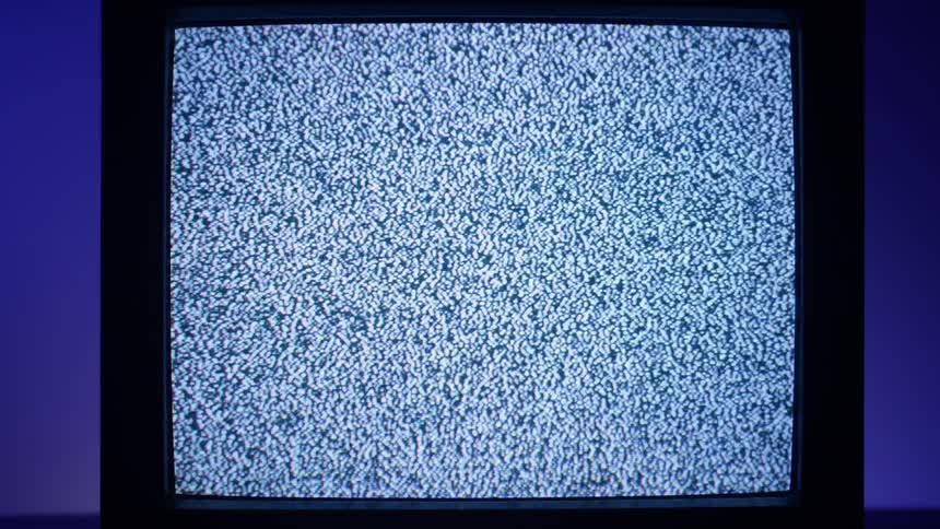 A television in a room with static on the screen with a wall in the background