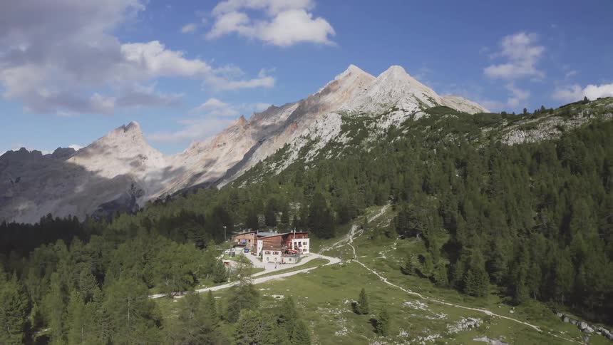 A landscape with cabins surrounded by trees with a mountain range the sky and clouds in the background